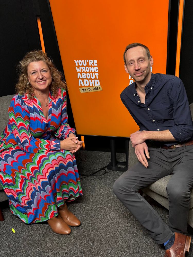 The image shows Katie Breathwick and Sam Pittis - the hosts of the You’re Wrong About ADHD podcast - sitting side by side in a studio smiling at the camera. 