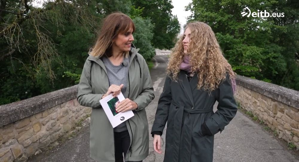 Ilaski eta Iosune harrizko zubi batetik ibiltzen, zuhaitzez inguratuta. Ilaski grisez jantzita doa eta esku artean Ahizpa beltza liburua darama. Iosunek gabardina ilun bat eta bufanda morea daramatza. Biek elkarri begiratzen diote eta irrribarre egiten dute. 