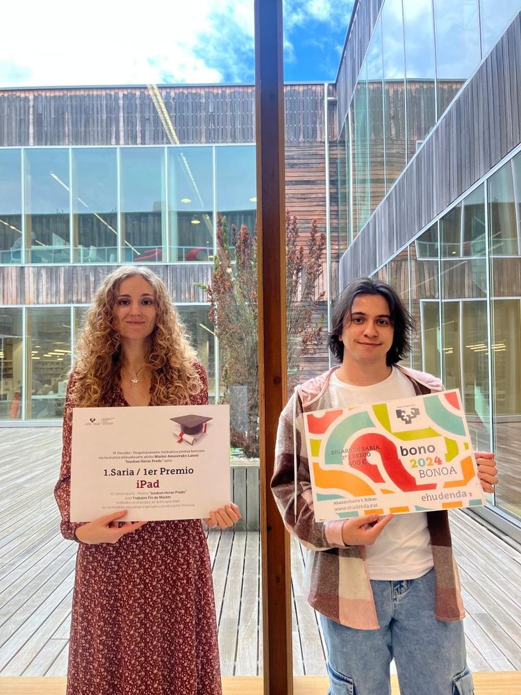 Iosune de Goñi eta Gorka Vergara Izaskun Heras Prado sarien banaketan, patio batera ematen duen leiho baten aurrean, diplomak eskuetan. Iosune ilehoria da eta soineko luze, granate bat darama. Gorkak bakeroak eta alkandora ireki bat daramatza eta kamerari irribarretsu begiratzen dio. 