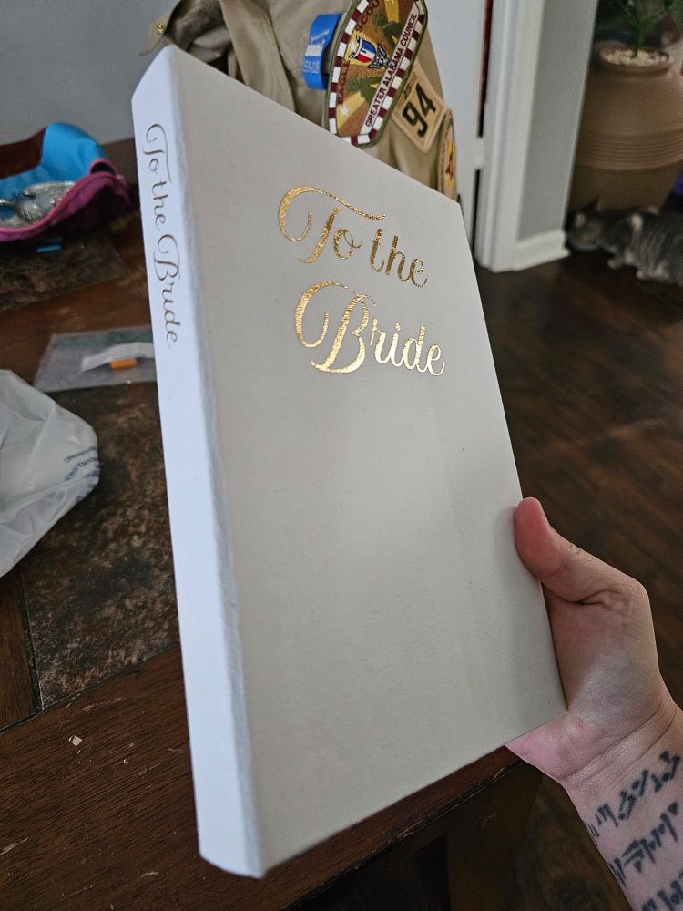 A shot of the newly rebound cookbook shows both the cover and spine. The cover is a bright white with the tile on both front cover and spine in gold script. 