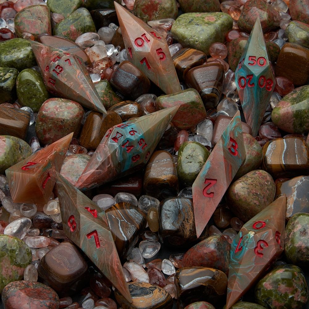 A set of crystal shaped dice resembling Lake Superior agate inked with red numbers lay amongst other polished stones.