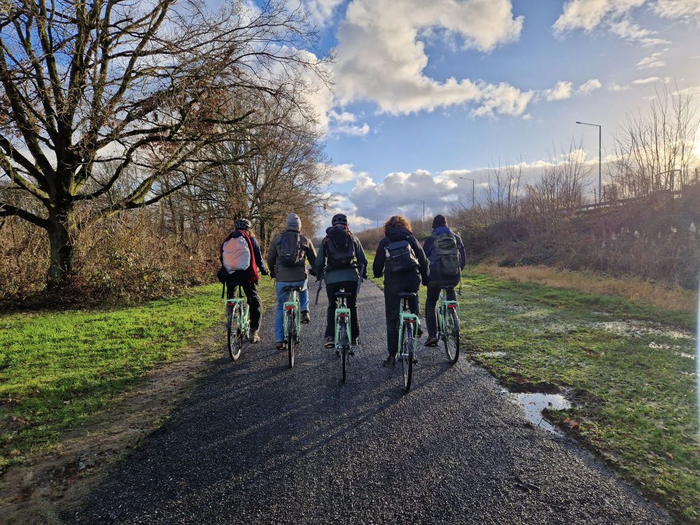Enkele enthousiaste collega's bij Trage Wegen fietsen op een recent ontharde straat die nu een trage weg is geworden.