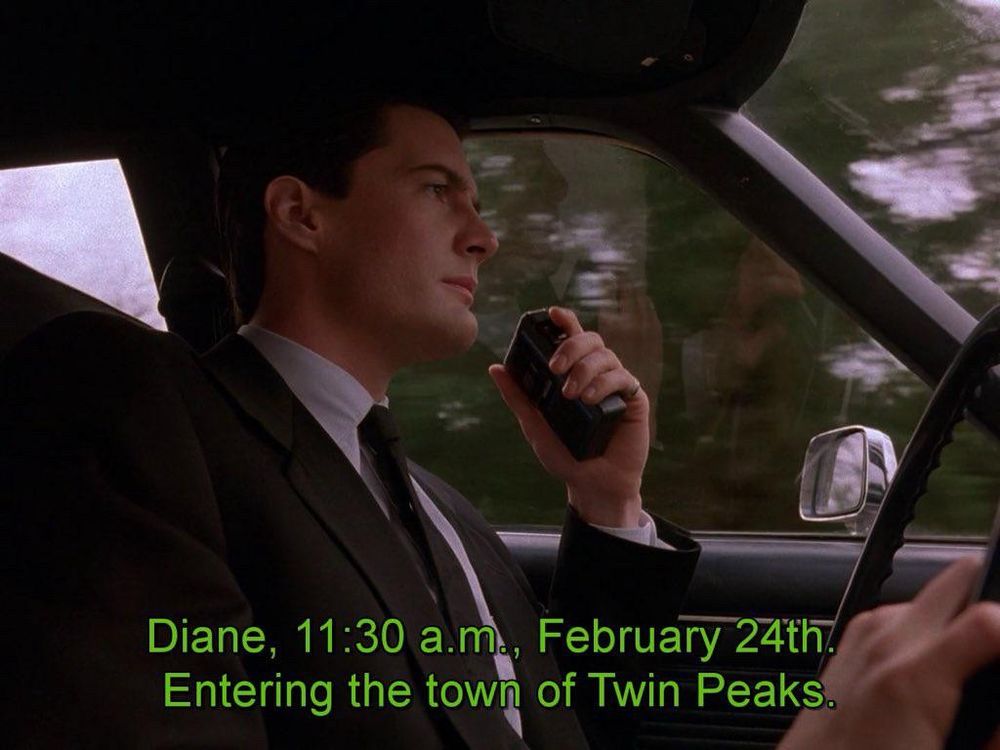 Hombre en traje conduciendo un coche mientras habla a una grabadora de mano. En la parte inferior de la imagen se reproducen en letras verdes lo que decía el personaje: Diane, 11:30 a m., February 24th. Entering The Town of Twin Peaks.