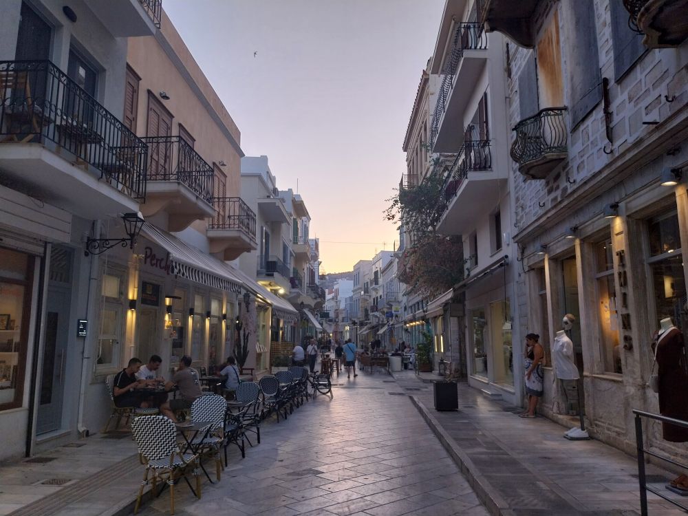 A cobbled street with old buildings on both sides and people sitting outside drinking. 