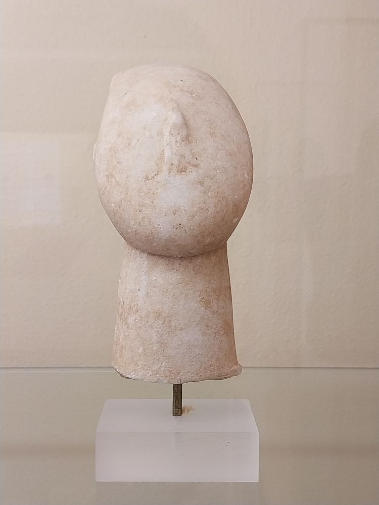 A small, white marble figurine depicting a head and neck. Only the nose is carved. 