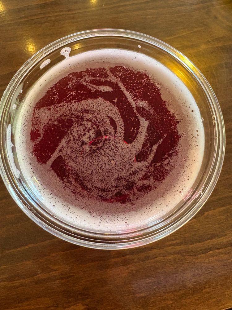 A top down view into a plastic cup of swirling cranberry-colored liquid with a light swirl of carbonation foam