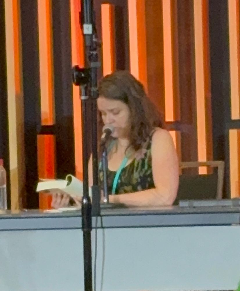 Erin Evans, seated at a table, reading from her novel. 