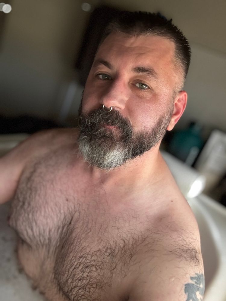 Bearded hairy man, shirtless in a bath with bubbles. 