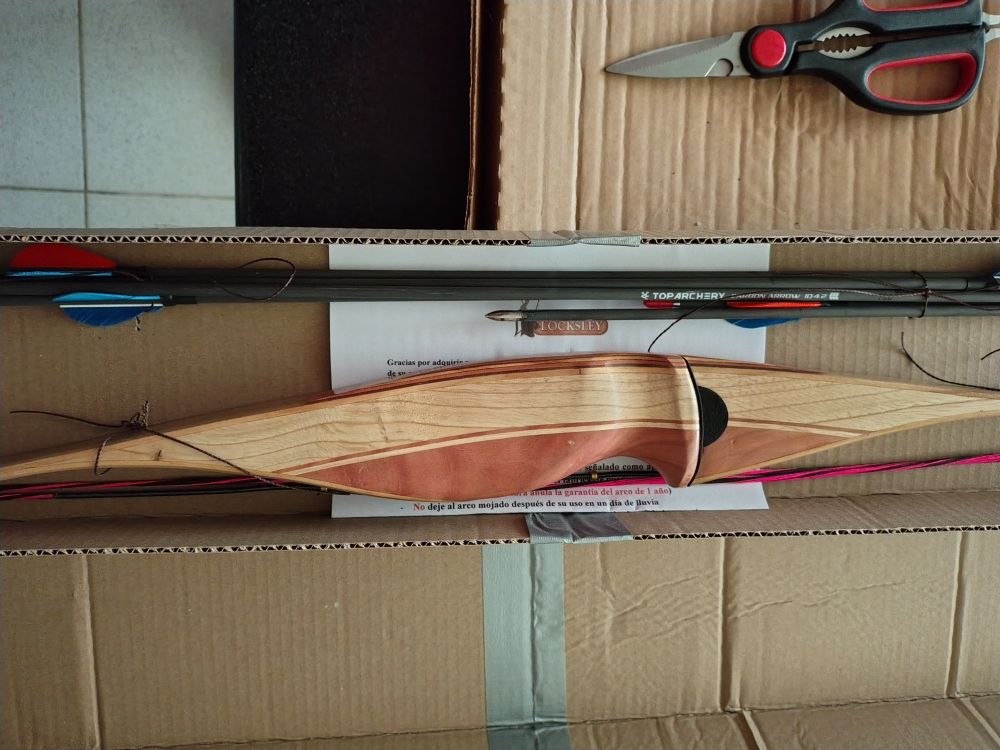 Close-up of the grip area of the bow from the side, showing the tan and pale reddish wood it's made from.