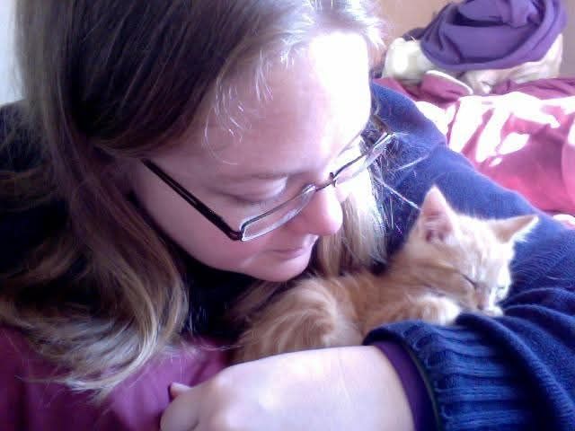Photo of me lying on my stomach on a bed and looking down at an orange kitten curled up and sleeping in the crook my my arm.