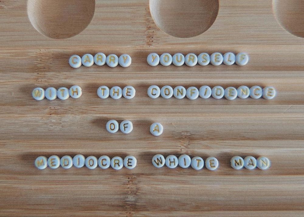 A photo of white, round letter beads laid out on a wooden letter board. 

They spell "carry yourself | with the confidence | of a | mediocre white man".