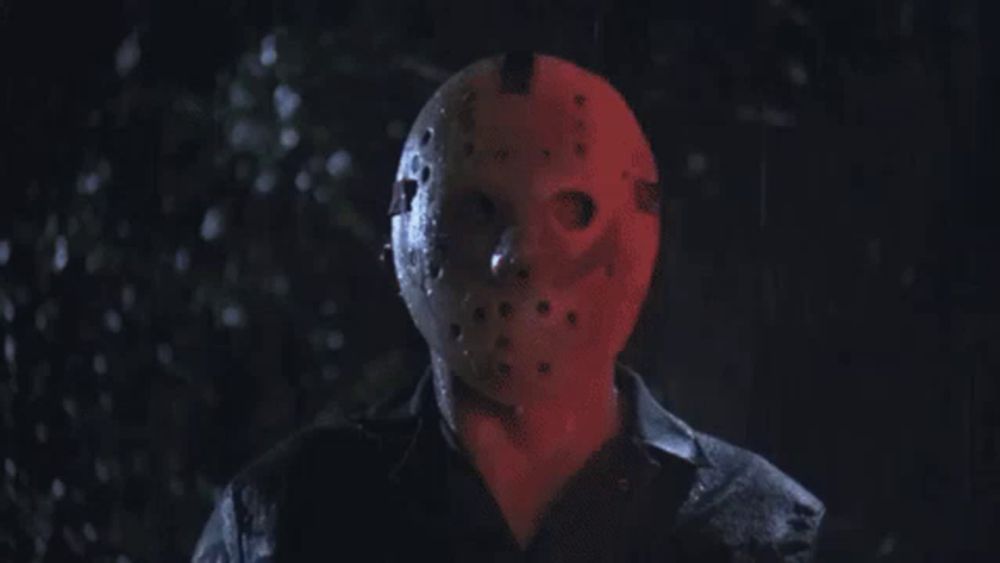 a man wearing a jason voorhees mask is standing in the dark in the rain .