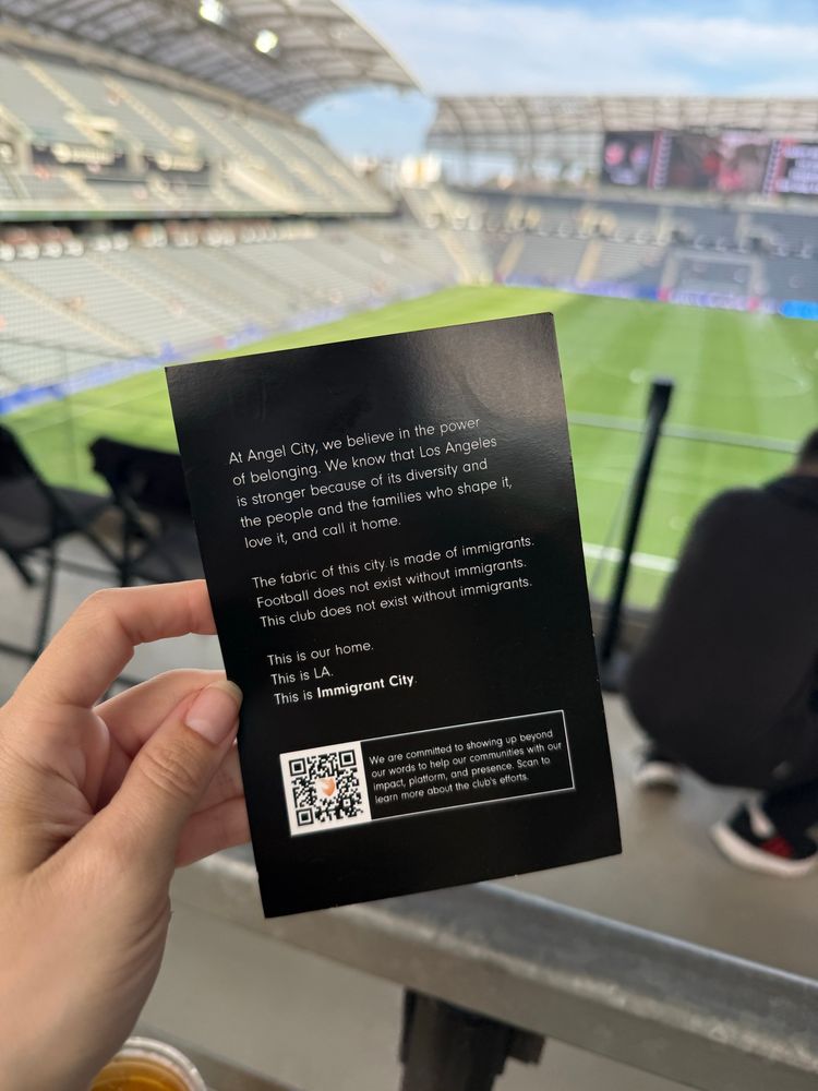 a handout card that says 

at angel city we believe in the power of belonging. we know that los angeles is stronger because of its diversity and the people and the families who shape it, love it, and call it home. the fabric of this city is made of immigrants. football does not exist without immigrants. this club does not exist without immigrants. this is our home. this is LA. this is immigrant city.