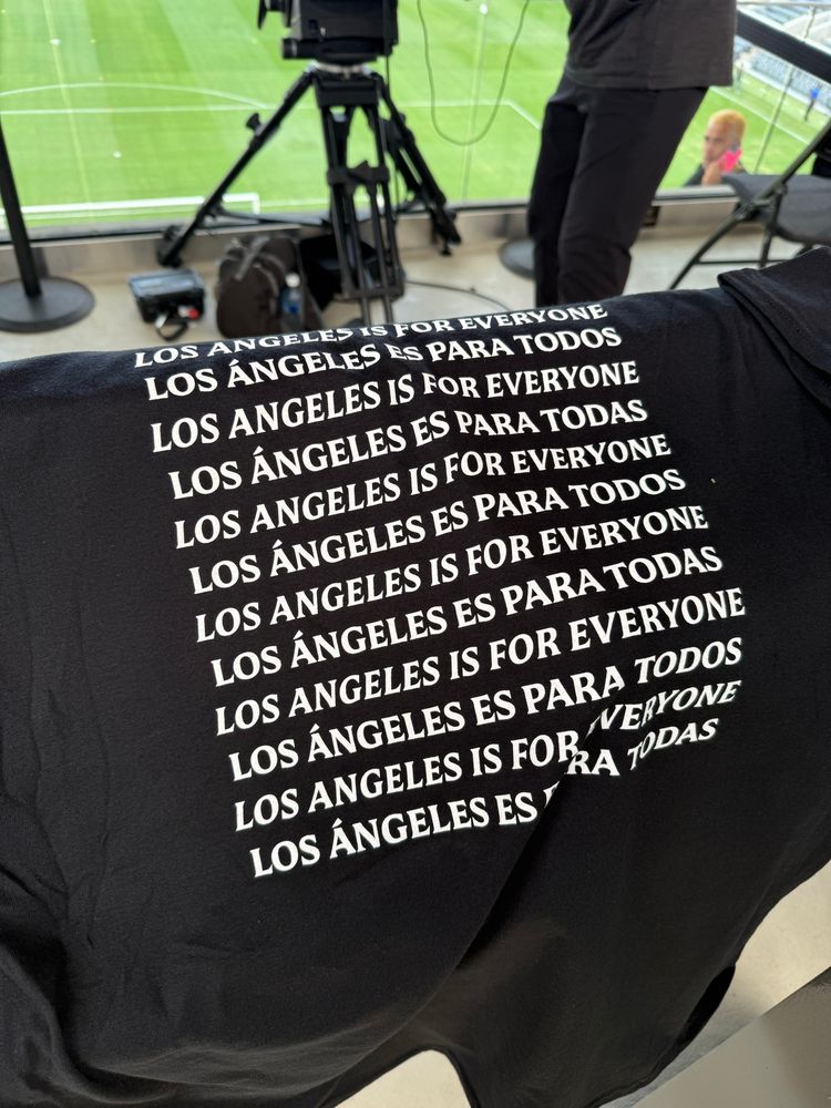 back of black shirt in white font that repeats over and over 

LOS ANGELES IS FOR EVERYONE 
LOS ÁNGELES ES PARA TODOS