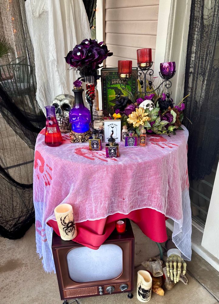 A table with a red cloth, covered in potion bottles & other assorted Halloween fare. 