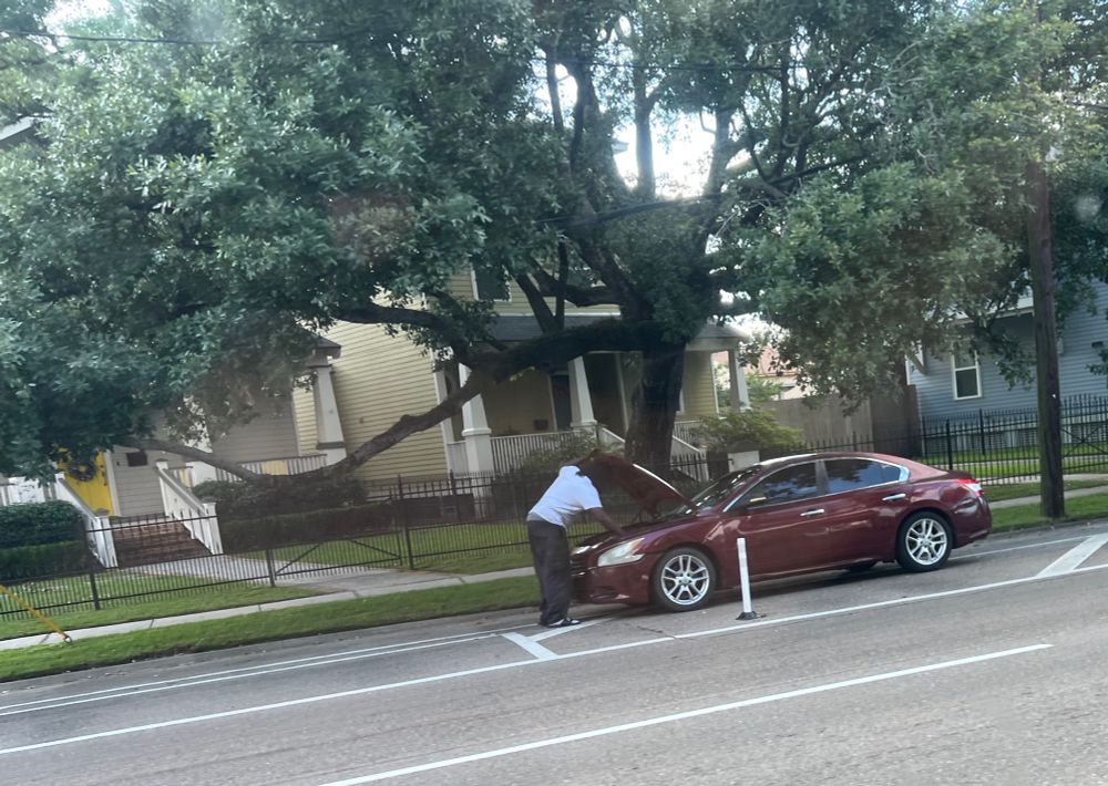 Guy standing over the hood of a maroon car parked in a “Protected” bike lane 