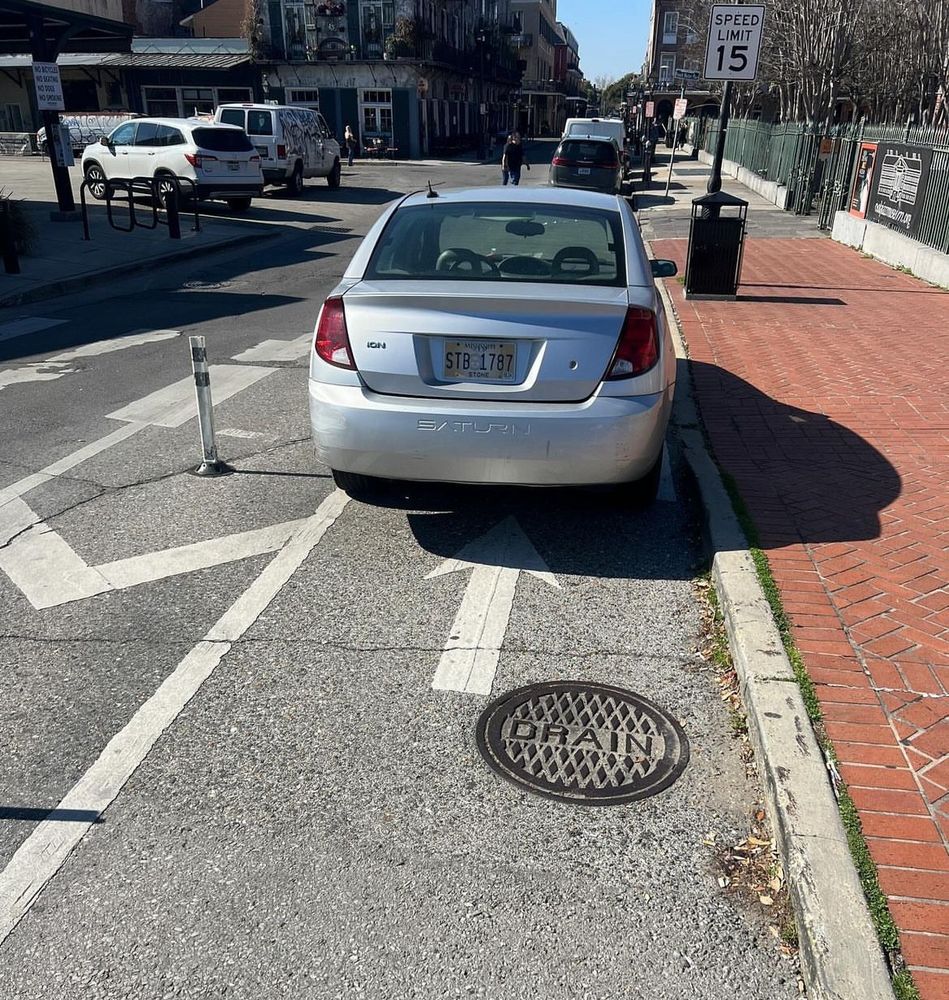 Silver Saturn sedan parked in a "protected" bike lane with flex posts doing nothing to prevent it