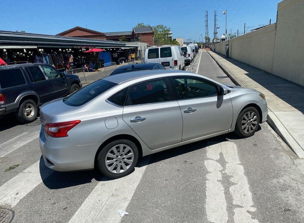 Silver sedan parked diagonally both in a crosswalk and across a bike lane. The double-whammy of idiot