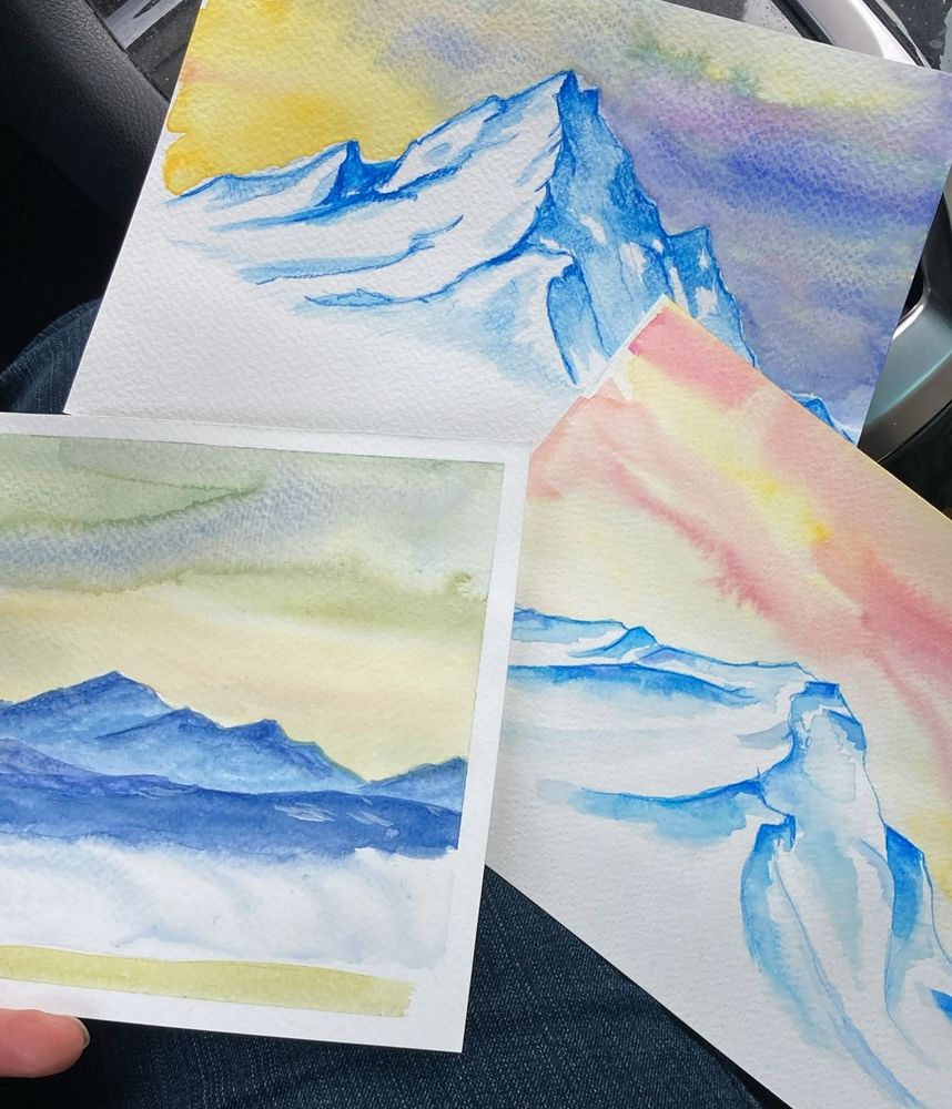 Three different views of mountains painted in watercolours. The mountains are mainly blueish, the skies yellow. 