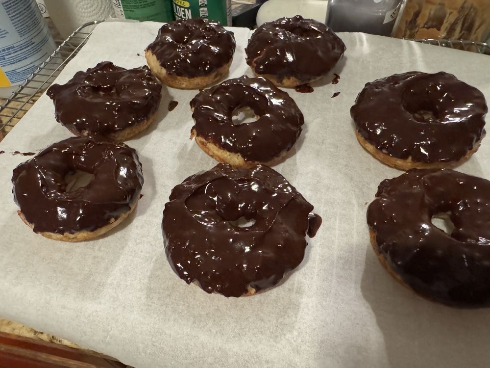 Eight chocolate donuts cooling on some parchment paper