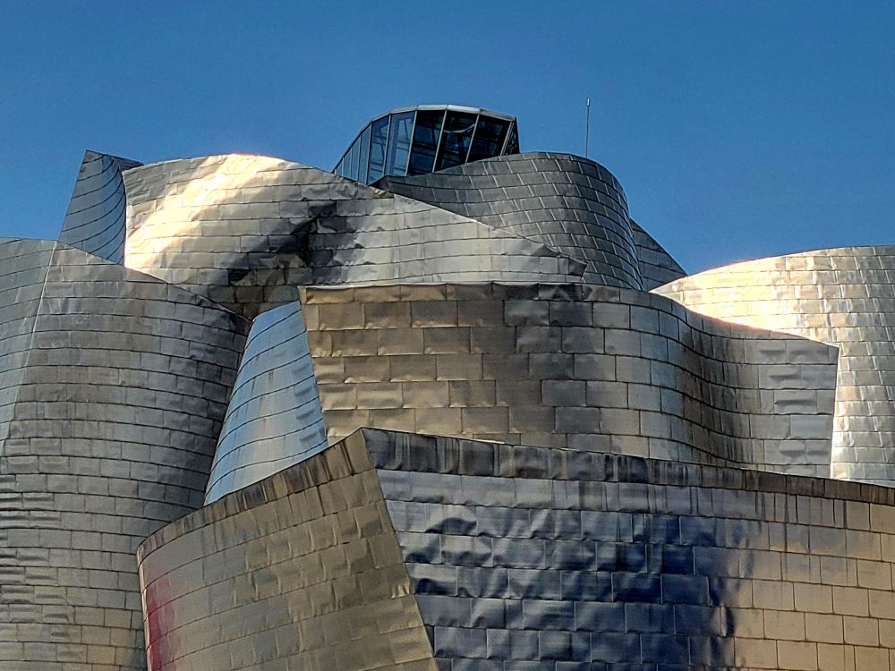 A direct view of the museum at ground level, with many shades of silver and brass playing in the light, all accentuated by dramatic curvature and sharp lines.