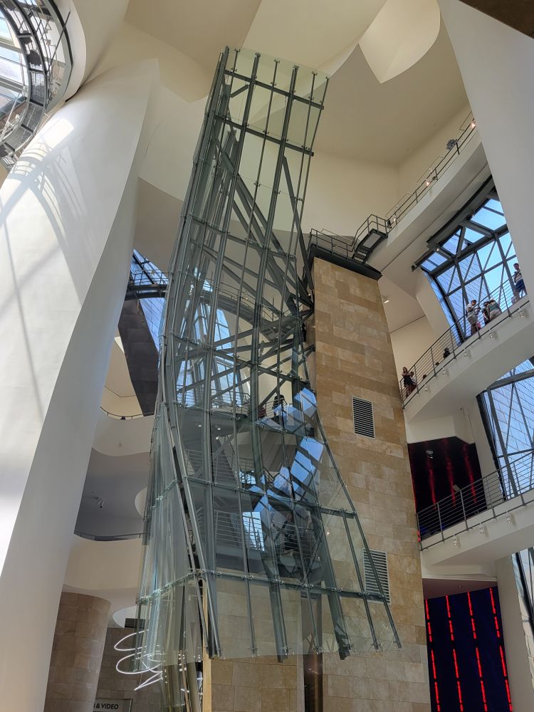 An interior view, looking up st soaring flat surfaces in white with bridges and a large metallic sculpture appearing to float in the interior span.