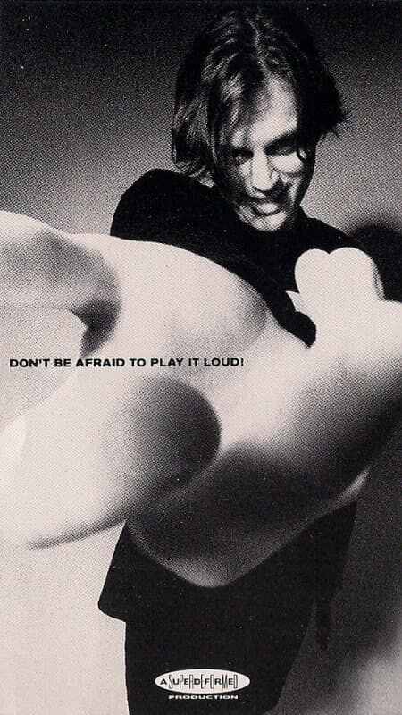 Musician Matthew sweet smiles and looks at the camera with his arm extended and hand miming the motion of turning up the volume while the caption reads: "don't be afraid to play it loud!"