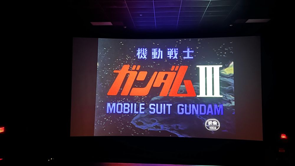 Photo taken inside of a theater. The screen displays the text of Mobile Suit Gundam III. It says "機動戦士ガンダムIII: MOBILE SUIT GUNDAM"