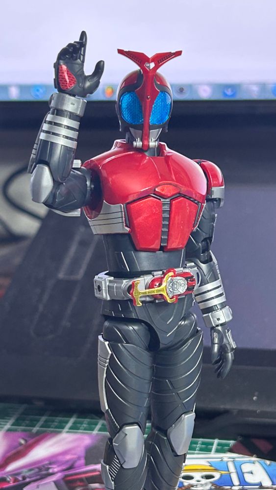Figure of Kamen Rider Kabuto performing his signature pose; he looks forward as he flexes his right elbow to a near 90° position, points his index finger to the sky with an open and visible palm.