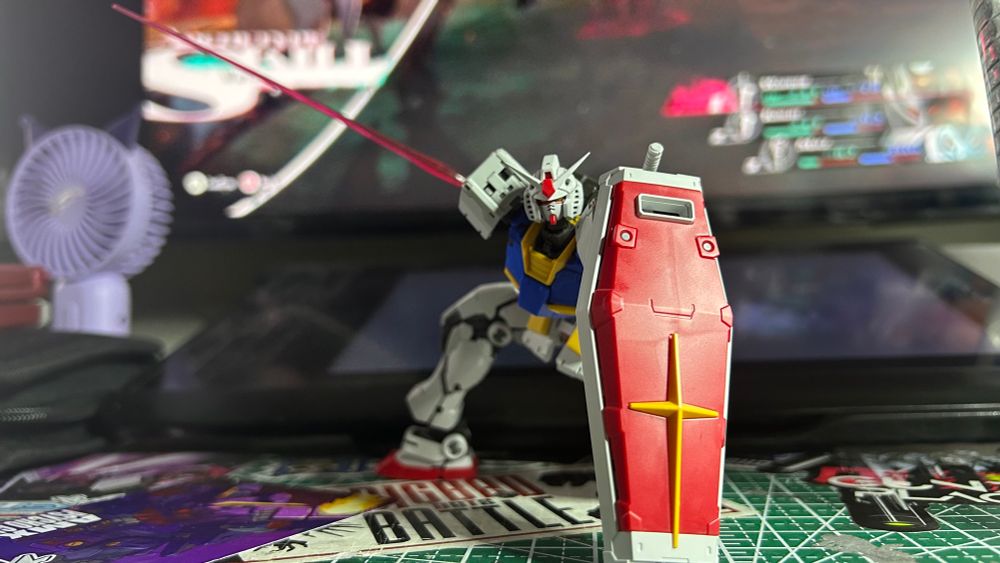 Classic Gundam in a superhero pose; left knee to the ground and the right leg posted up in the back, holding its shield down to the ground on its left arm and its beam saber extended behind the Gundam in its right hand.