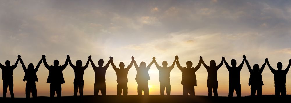 Group of people with raised hands in front of sunset