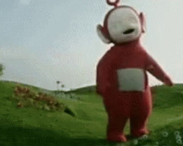 a red and white teletubbies character is standing in a field .