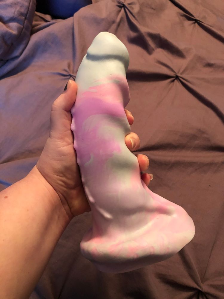 Leth holding their favorite toy, a Pleasure Forge Hook Horror, which their hand doesn’t close around