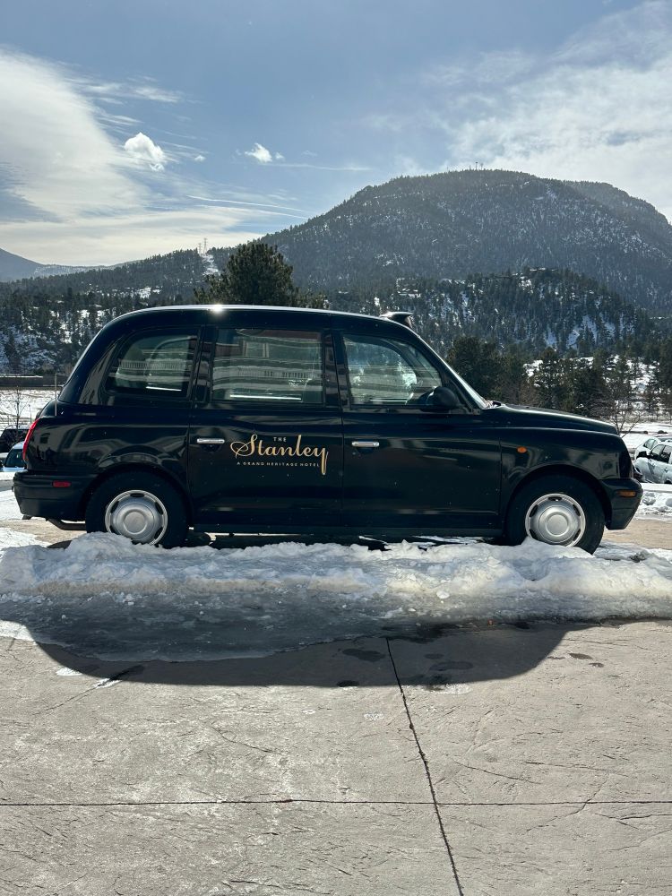 Small black car that looks to be a PT Cruiser. The back passenger door is emblazoned with The Stanley Hotel logo.