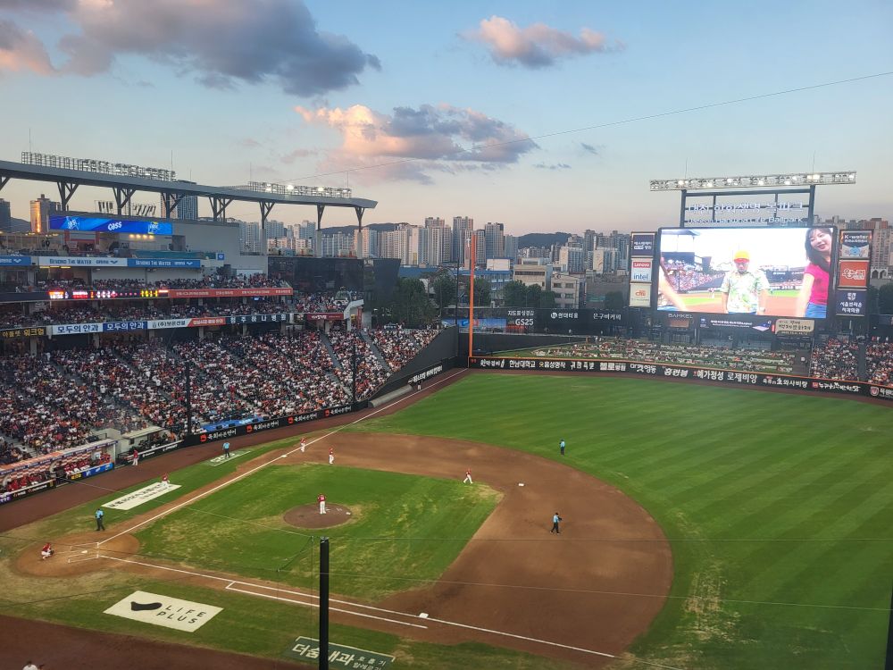 Photo of Hanwha stadium from above first base. On the big screen is a middle aged-ish Korean man dressed as a Saja Boy from Kpop Demon Hunters