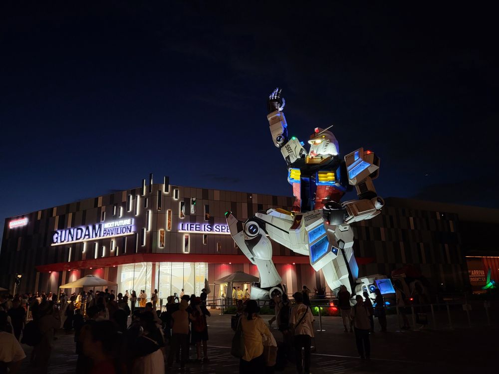 The life size gundam at Osaka Expo 25 at night with the pavilion behind him.