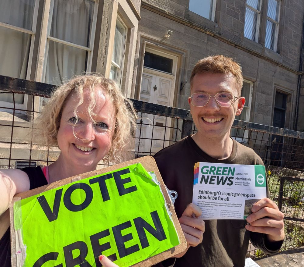 Kate and Ben sitting in the sun on a wall in Marchmont, holding up a Vote Green clipboard and a copy of Green News
