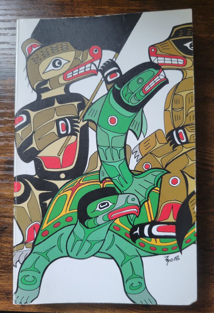 The cover of a paperback book. The cover art features a turtle, salmon, coyote (?), and bear in the style of Pacific Northwest Coast formline art on a white background. The bear is waving a black flag. There is no title on the book cover 