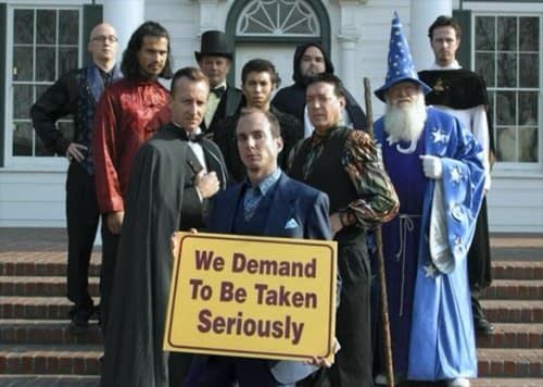 Screenshot from Arrested Development showing Gob and a group of magicians standing on the steps of a building with the sign "We demand to be taken seriously"