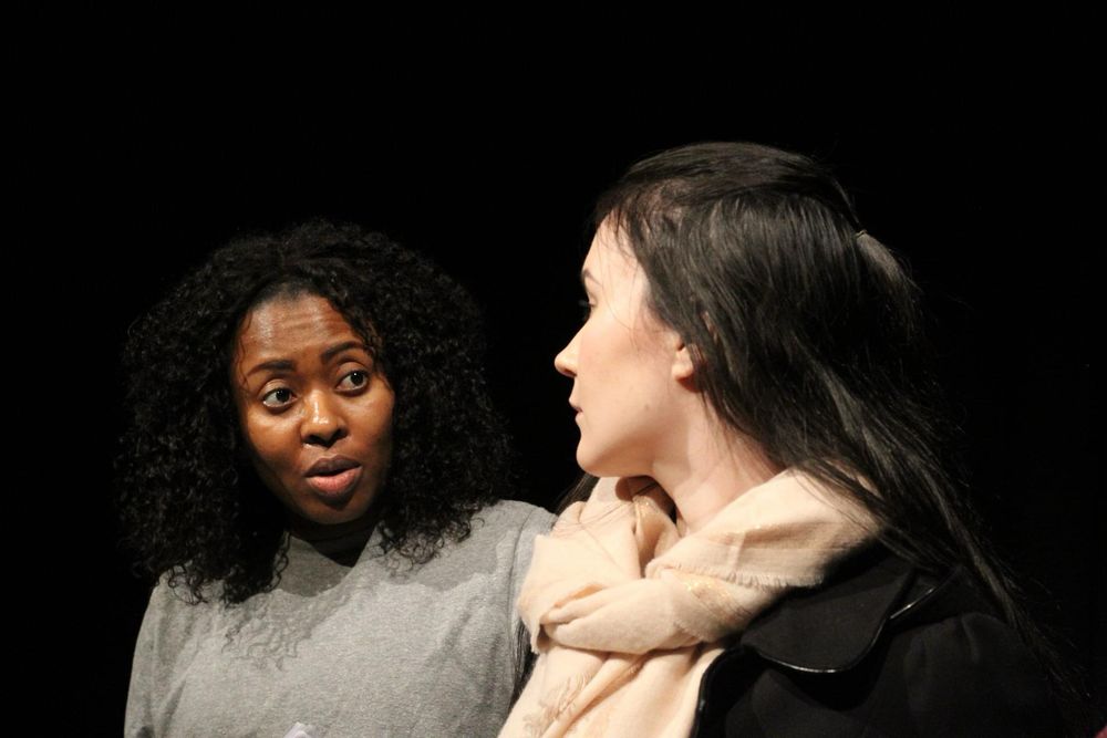 A woman is talking to another woman. The first woman face is clearly seen while the other is in profile turned looking at the woman talking.
