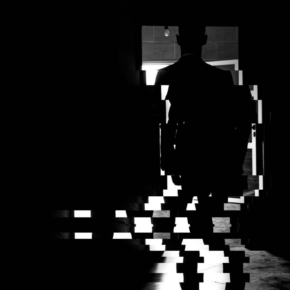 A silhouette of a man in an open doorway the bottom of his legs are sliced and jutted. The picture is in black-and-white.