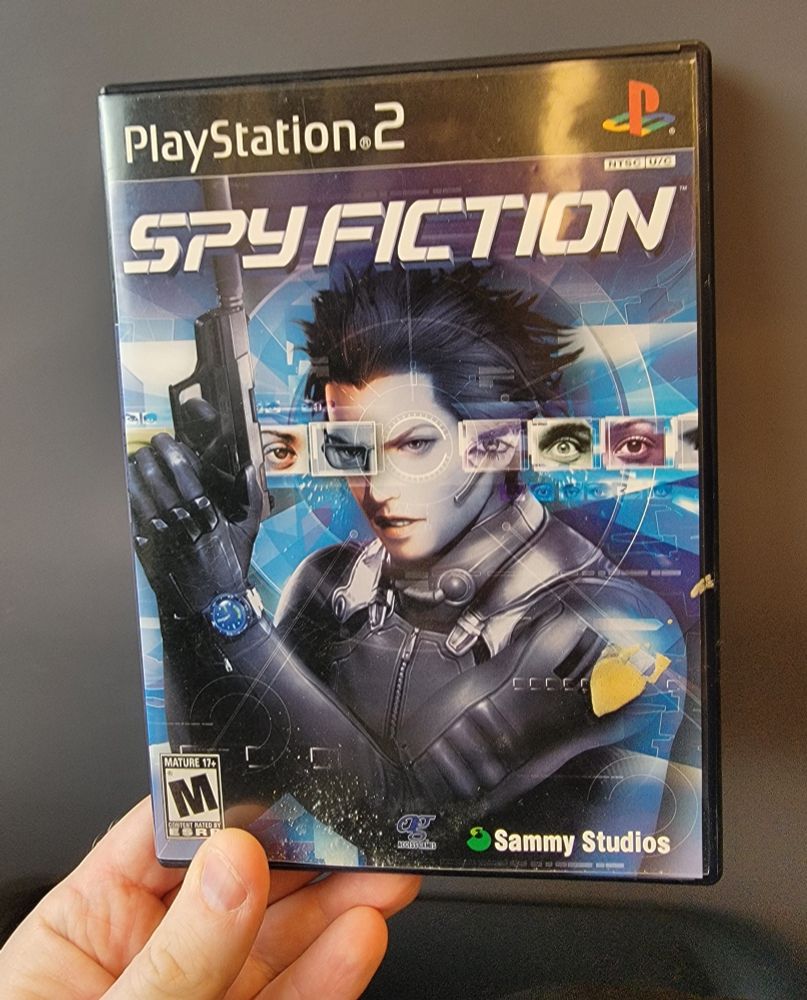 My hand holding a copy of Spy Fiction for the PS2 against a dark grey backdrop