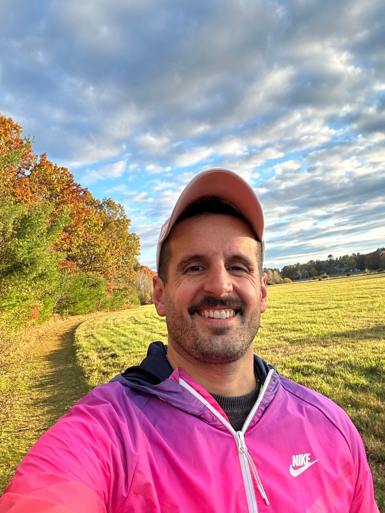 Selfie in a pink windbreaker against a fall sky