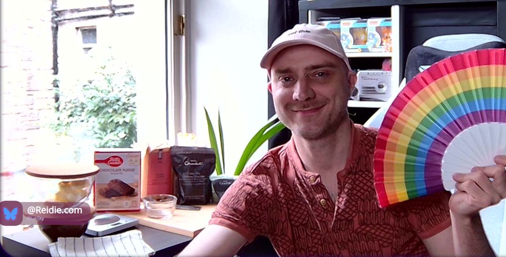 Reidie (tired and bald) is seen holding a rainbow hunty pride fan, sitting beside baking ingredients, there's also a TalkBoy from Home Alone 2 and cosplaying ducks seen on a shelf