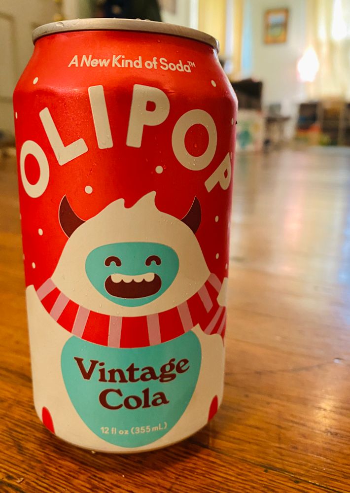 A photo of Olipop soda can, vintage cola flavor 
On a wood floor with a blurry background 
