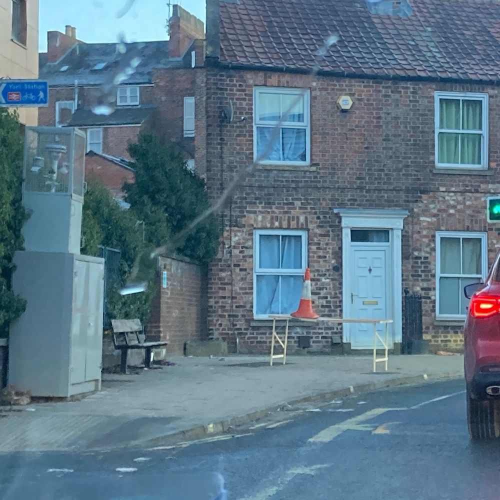 A street in York. In the middle of the path is a decorator’s table with a traffic cone o ok avec on top. No explanation. 