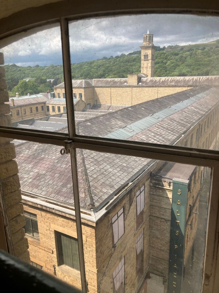 A view out of the window towards a tower with hills in the background. In the foreground is the Victorian factory roof of the mill. 