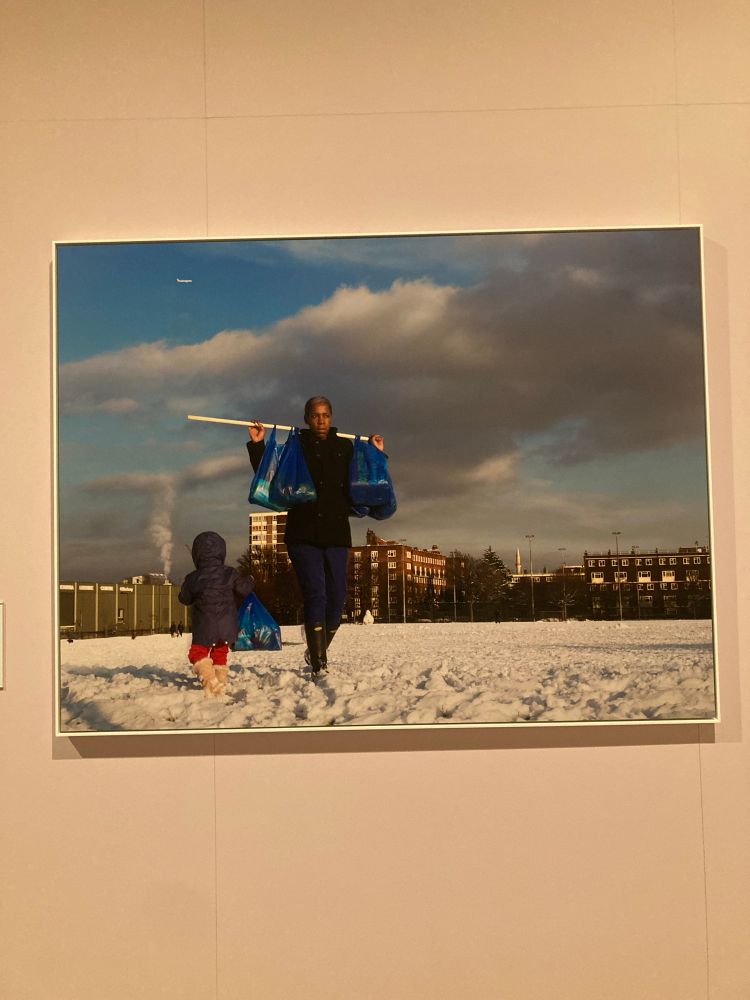 A work by Hannah Starkey, of a woman walking along in the snow next to her young child with a city in the background. 