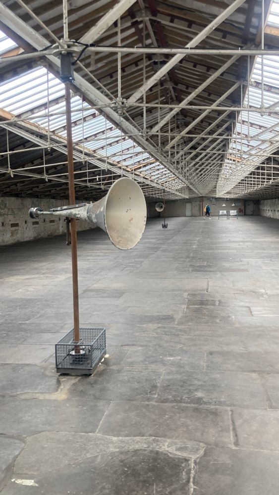 A megaphone on a stand. It’s just a picture but the megaphone spins round and plays beautiful music, there are two more in he background of this industrial space. 