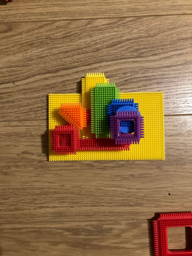 An abstract ‘rainbow’ made in sticklebricks on a bright yellow sticklebrick board. 
